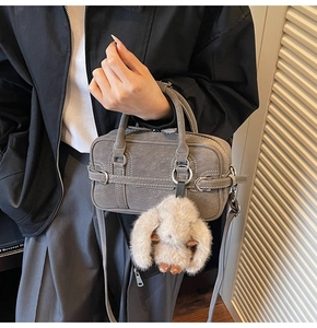 Close-up of a dark grey suede handbag with silver buckles and a cute plush rabbit charm