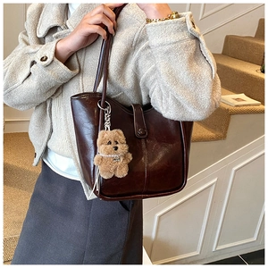 Detail of dark brown leather tote bag with a cute plush bear charm on white stairs