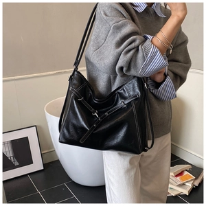 Detail of black leather tote bag featuring contrast white stitching and silver hardware