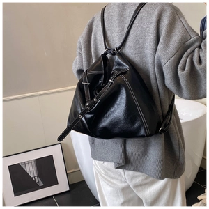 Detail view of black glossy leather bag with white contrast stitching on model