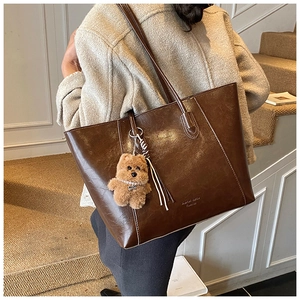Detailed texture of brown oil-wax leather tote bag with a cute plush bear charm