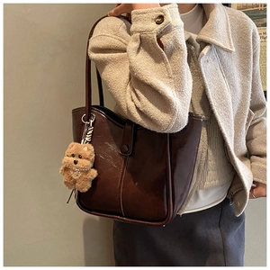 Side view of deep brown faux leather tote bag with plush bear charm on model shoulder