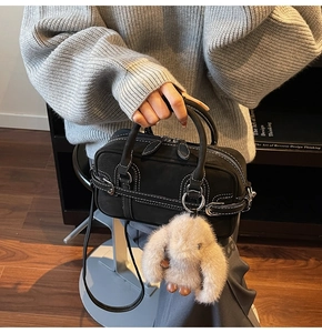 Detail of black matte handbag with white stitching and a cute plush rabbit pendant