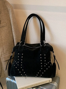 Chic black tote bag with silver rivets and dual straps on a suitcase for commuting