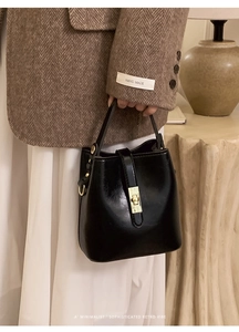 Detail of a black glossy bucket bag featuring a sophisticated gold square twist lock