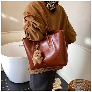 Detail of red-brown leather tote bag with plush bear charm and sleek shoulder straps