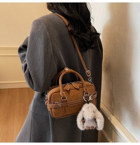 Detail of brown suede crossbody bag with plush bunny charm and adjustable leather strap
