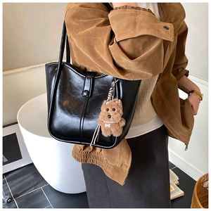 Detail of black wax leather tote bag with brown plush bear charm worn by a model
