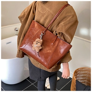 Detail of vintage brown tote bag with smooth texture and cute plush bear charm accessory