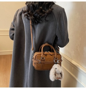 Detail view of a vintage brown leather crossbody bag with a plush bunny charm on a coat