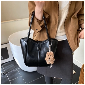 Close-up of black glossy leather tote bag with a brown teddy bear charm on the shoulder