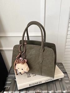 Sac à main vert olive en similicuir avec un pendentif peluche blanc sur une valise