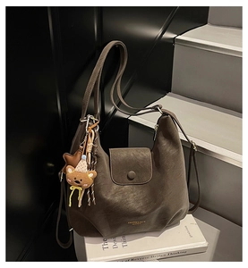 Detail of dark brown leather hobo tote bag featuring a cute bear plush charm on strap