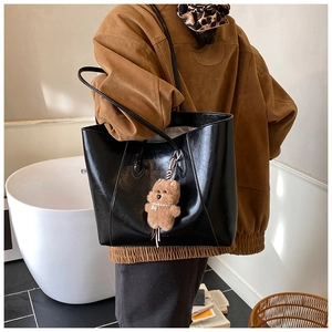 Detail of black large capacity tote bag with long straps and brown plush bear charm