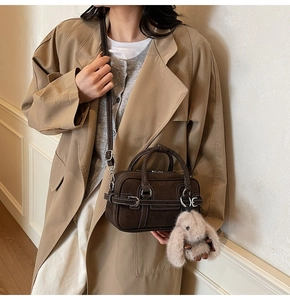 Detail of dark brown suede Boston bag with silver buckles and a cute plush rabbit charm