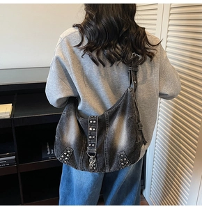 Detail of oversized washed denim hobo bag featuring silver punk rivets and metal buckles