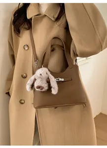 Brown leather bucket bag with silver clasp and plush rabbit charm detail on a wool coat