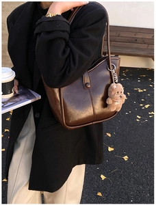 Detail view of a vintage brown shoulder bag with a plush bear charm on an autumn street