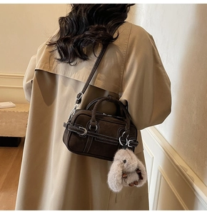 Detail of dark brown suede crossbody bag with contrast stitching and rabbit charm