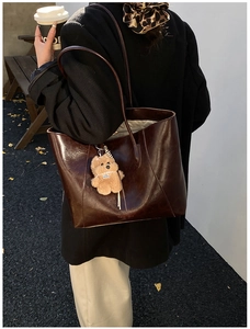 Detail of dark brown tote bag with bear charm worn by a model in outdoor setting