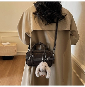 Detail of dark brown suede Boston bag with white stitching and plush rabbit charm