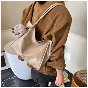 Detail der beigen glänzenden Hobo-Tasche mit flauschigem Anhänger und Goldakzenten