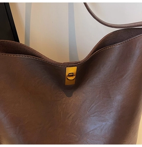 Macro detail of dark brown leather bucket bag with retro golden metal twist lock closure