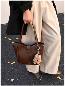 Detail of dark brown leather tote bag featuring a plush bear charm and sleek vertical stitching