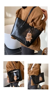 Detail of black large capacity tote bag featuring glossy leather and plush bear pendant