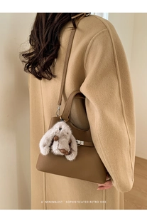 Détail du sac seau en cuir marron foncé avec un charmant lapin en peluche sur un manteau