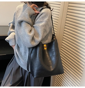 Detail of black bucket bag featuring a polished gold square lock and adjustable strap