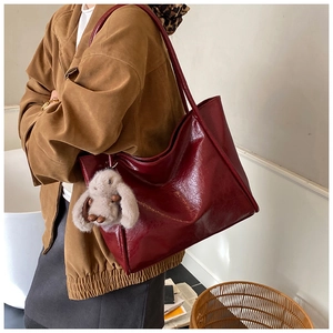 Detail der dunkelroten Lackleder-Tote Bag mit Plüsch-Kaninchen-Anhänger am Schultergurt