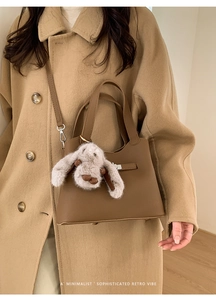 Close-up of brown pebbled leather bucket bag with a cute plush bunny charm and shoulder strap