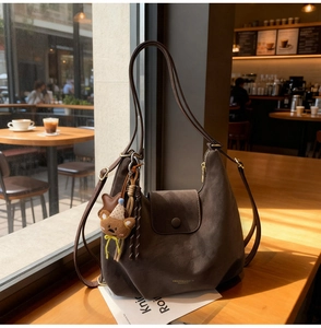 Detail of dark brown matte tote bag with teddy bear charm on a warm cafe windowsill