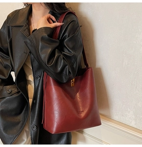 Detail of burgundy bucket bag with gold twist lock worn by a model in black coat