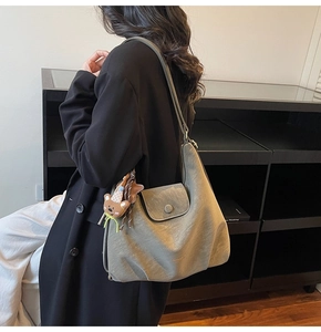 Close-up of a large grey leather tote bag with a cute bear pendant on a model's shoulder