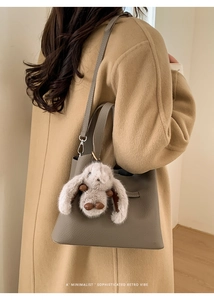 Close-up of leather bucket bag with plush rabbit pendant and minimalist texture