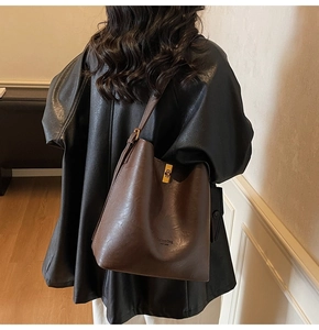 Detail of dark brown bucket bag with gold clasp and textured synthetic leather finish