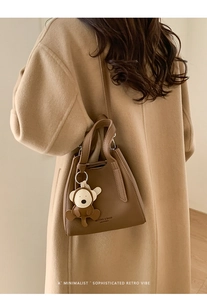 Brown leather bucket bag with monkey charm shown on a camel wool coat model