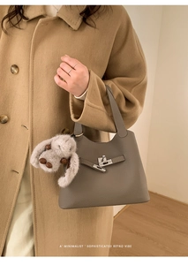 Détail d'un sac seau en cuir gris avec fermoir rotatif argenté et breloque lapin en peluche