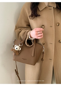 Detailed view of dark brown pebbled leather bucket bag with a cute bear charm and long strap