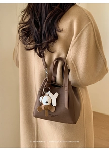 Close-up of brown litchi pattern leather bucket bag with cute cartoon monkey charm