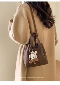 Detail of dark brown leather bucket bag with bear pendant worn with a stylish winter coat