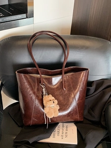 Vintage large capacity dark brown tote bag with bear charm on a leather chair