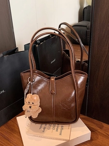 Retro dark brown glossy leather tote bag with plush bear charm on a minimalist setup
