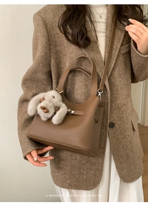 Detail of a brown leather bucket bag featuring a vintage buckle and a plush rabbit charm