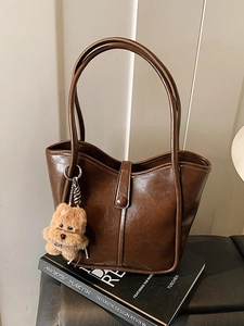 Retro dark brown leather tote bag with plush charm on Andrew Martin interior design book