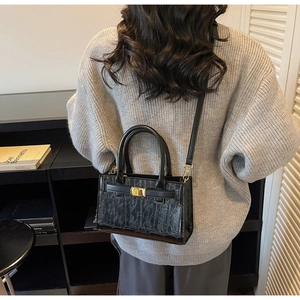 Detail of black crocodile texture handbag with gold lock on a gray knit sweater