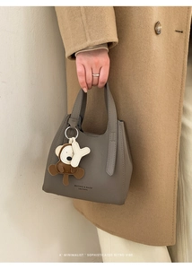 Detailed view of grey leather bucket bag with cute monkey pendant and brand lettering
