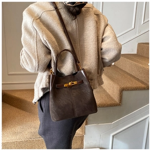Detail of suede bucket bag with gold metal lock and brown leather trim on stairs